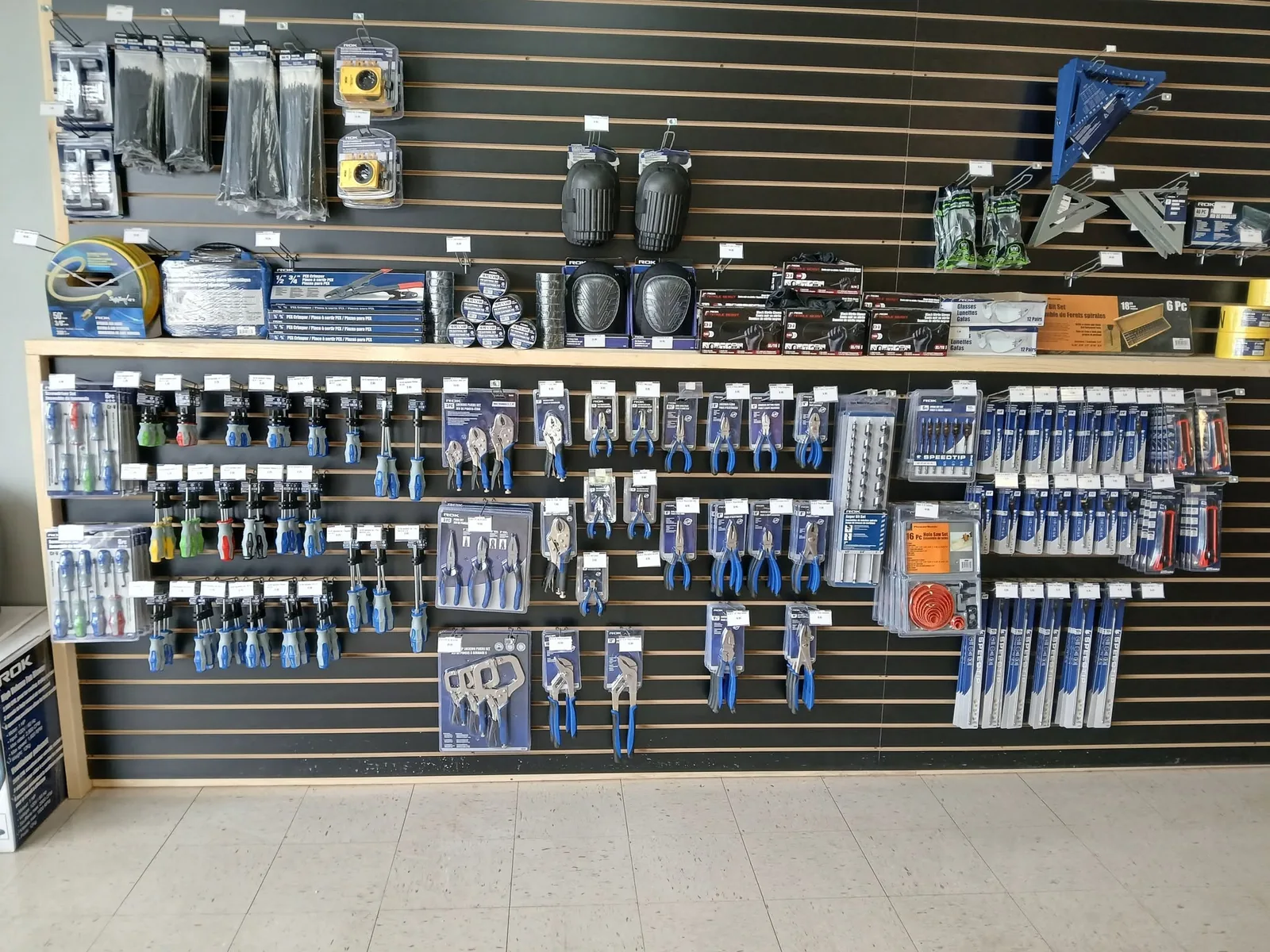 Intérieur du magasin : mur d'outils et de quincaillerie sur panneau à lattes.